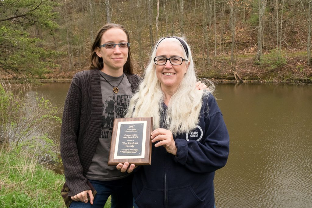 Two women holding an award plaque next to a pond